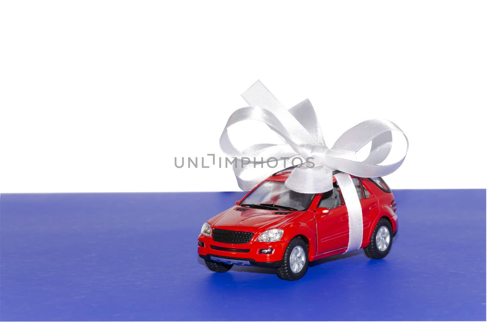 Red car, tied with white ribbon on a blue desktop on a white background