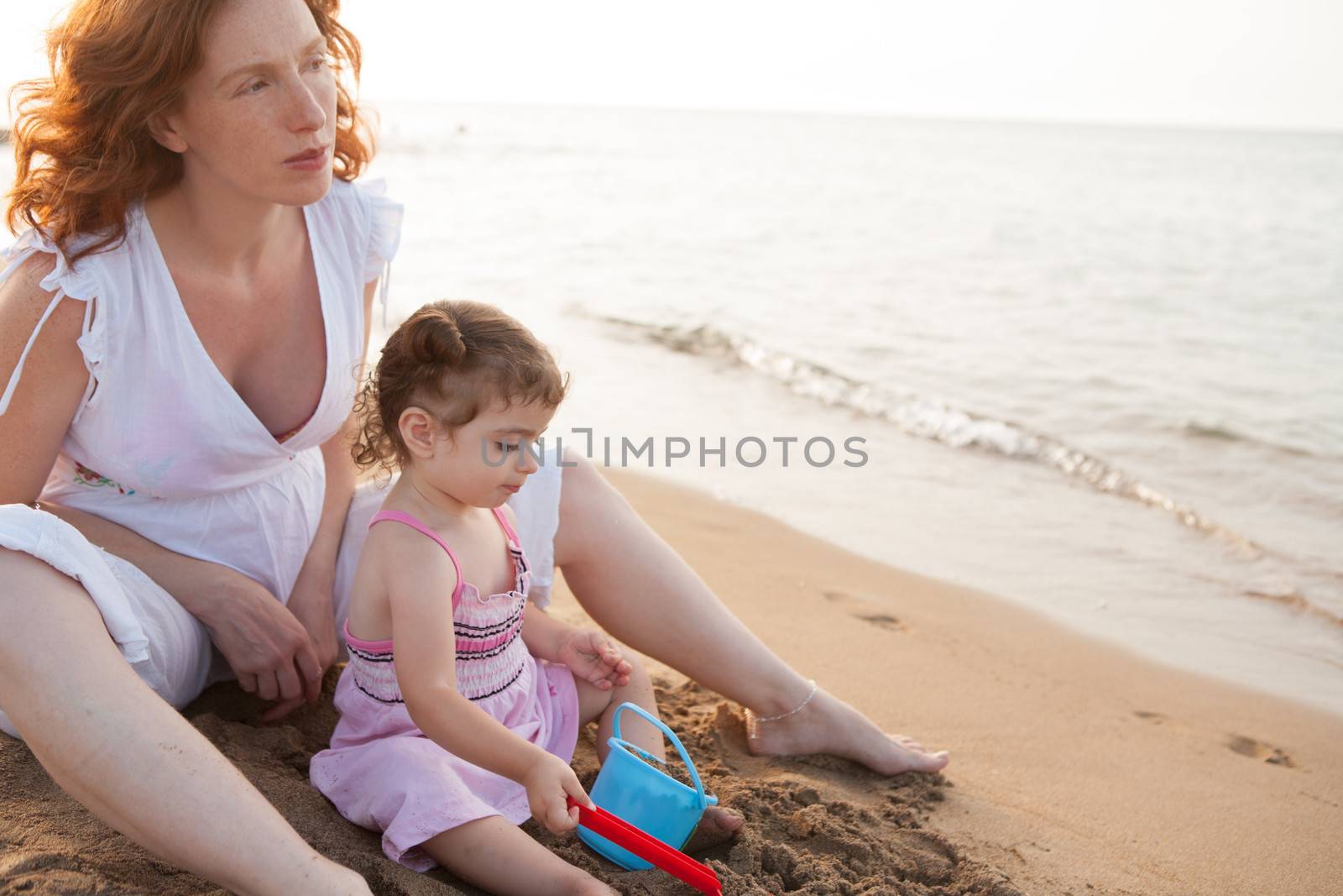 pregnant mother and daughter playing in beach sand by lunamarina