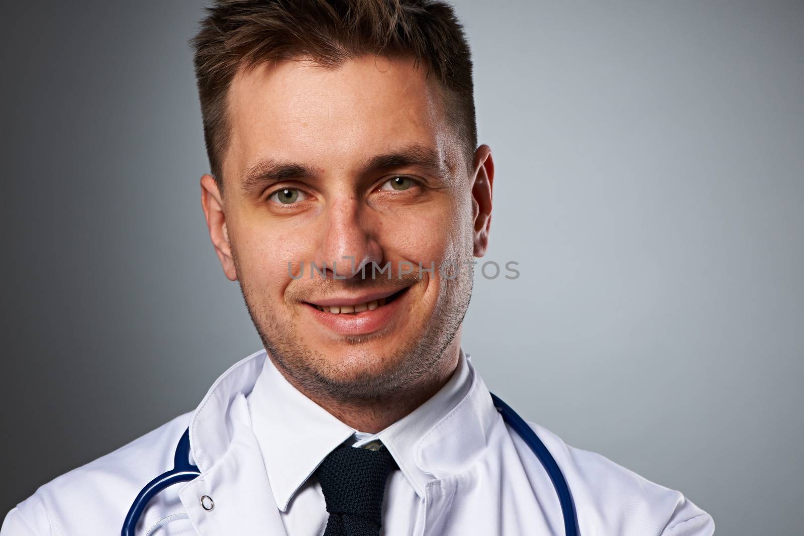 Medical doctor with stethoscope portrait against grey background 