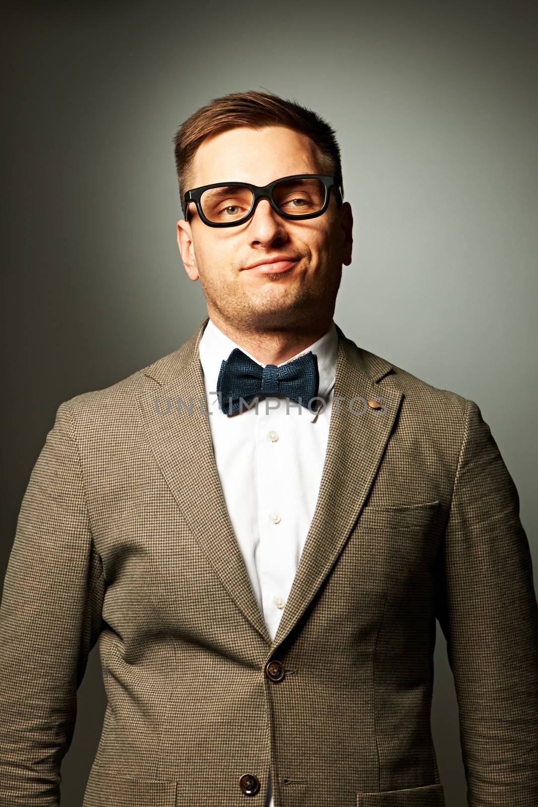 Confident nerd in eyeglasses and bow tie against grey background