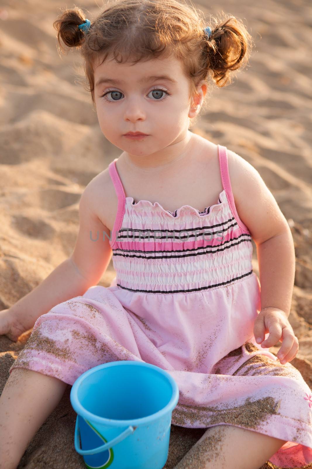 Blu eyes brunette toddler girl playing with sand in beach by lunamarina