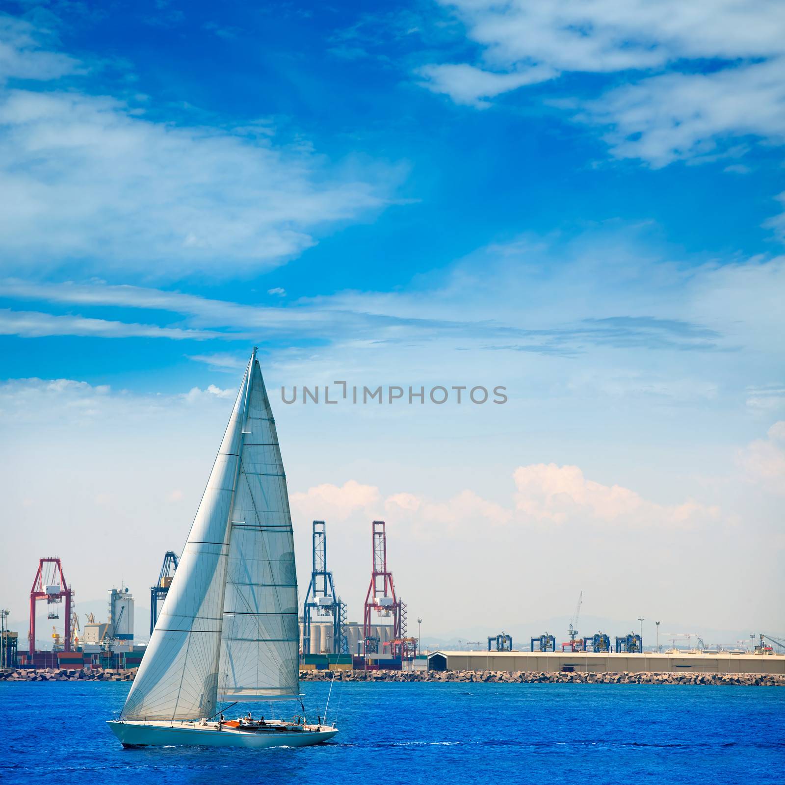 Valencia city port with sailboat and cranes in background by lunamarina