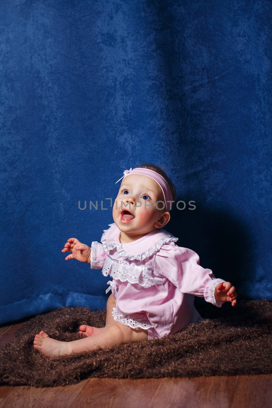 Pretty blue-eyed girl in a pink dress sitting on the floor