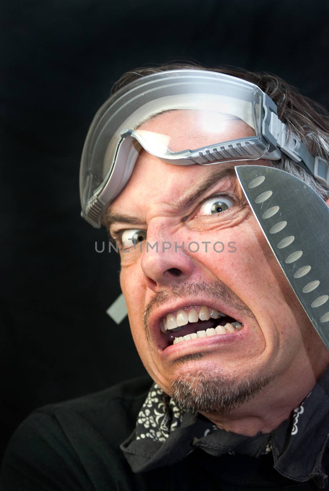 Close-up of a crazy man wearing goggles with a knife loking afraid.