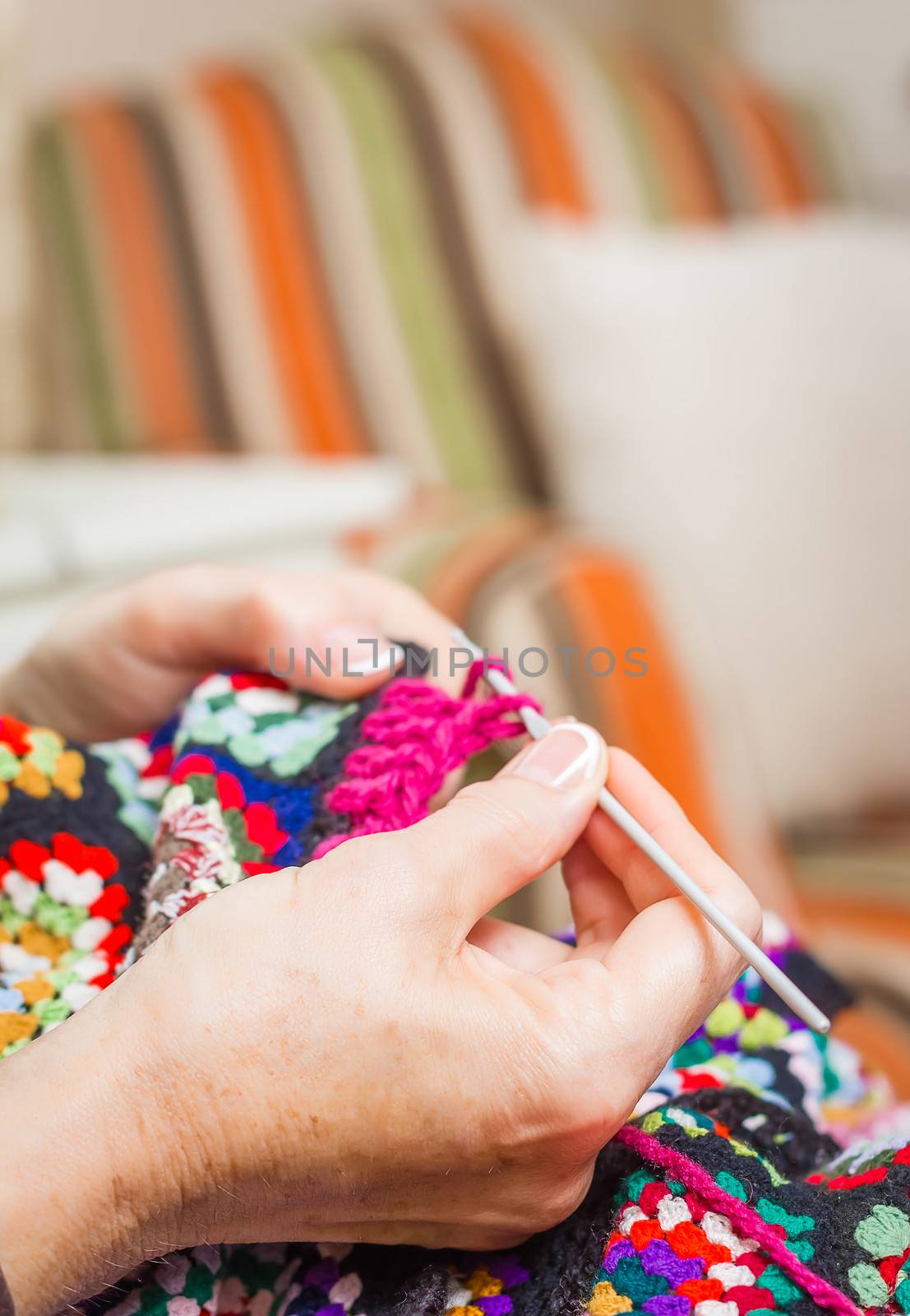 Hands of senior woman knitting a vintage wool quilt with colorful patches. Selective focus over hand in the foreground.