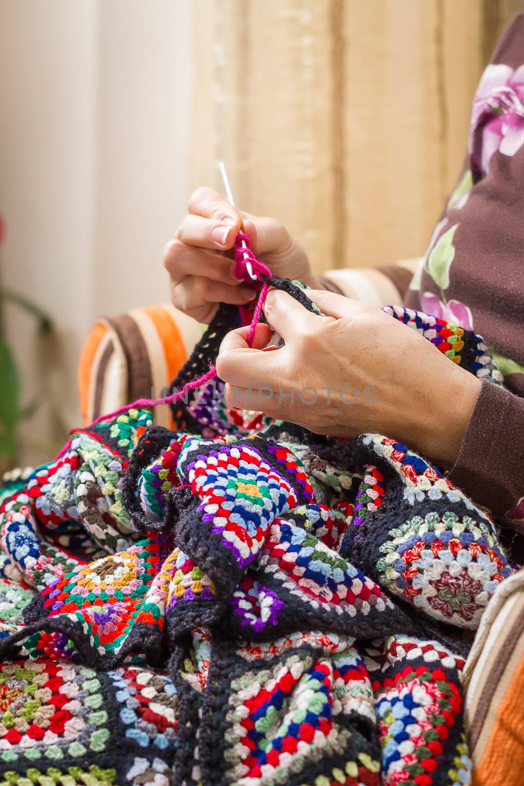 Hands of senior woman knitting a vintage wool quilt with colorful patches