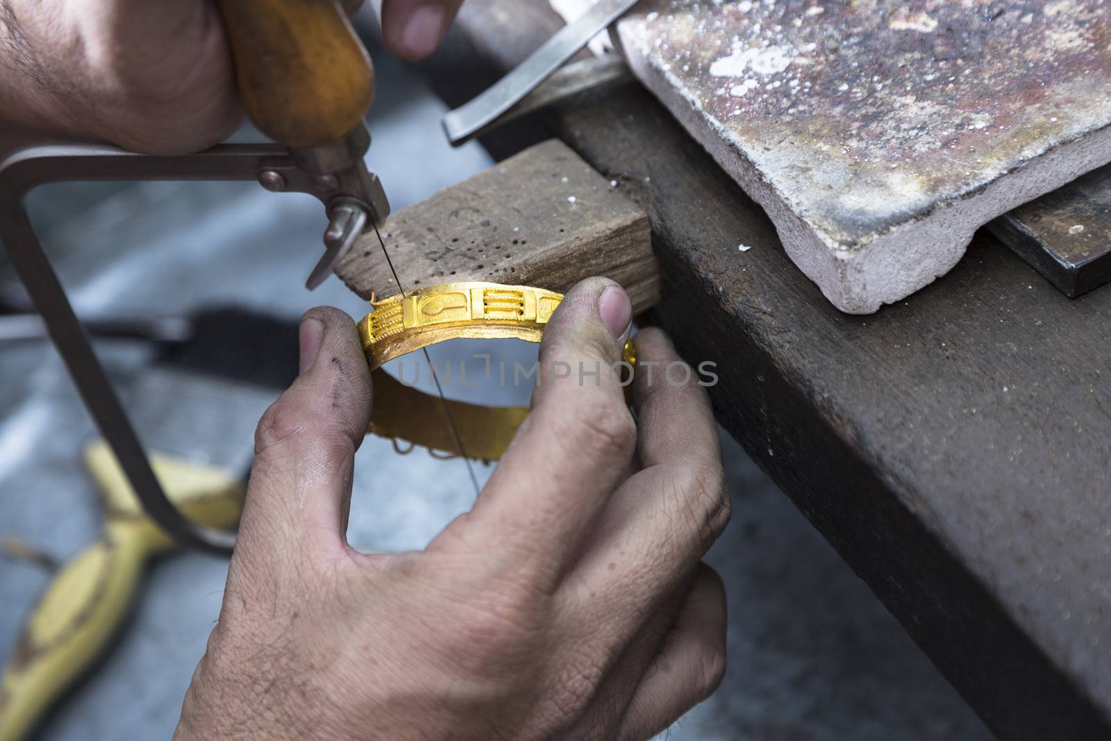 Close up of Jeweler crafting golden bangle with flame torch.