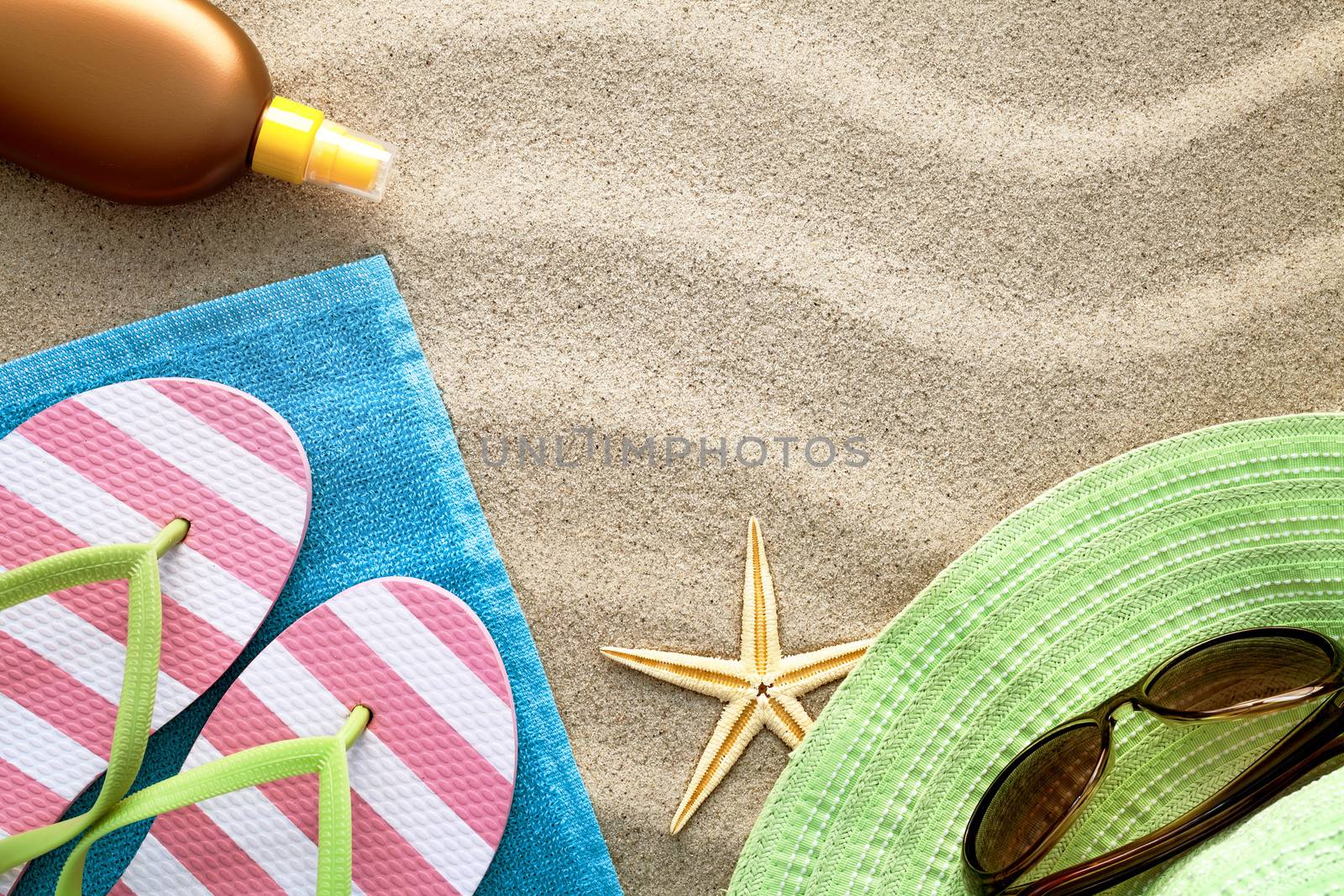 Sandy beach background with towel, flip flops, hat, sun glasses, suntan oil and starfish. Summer concept. Top view