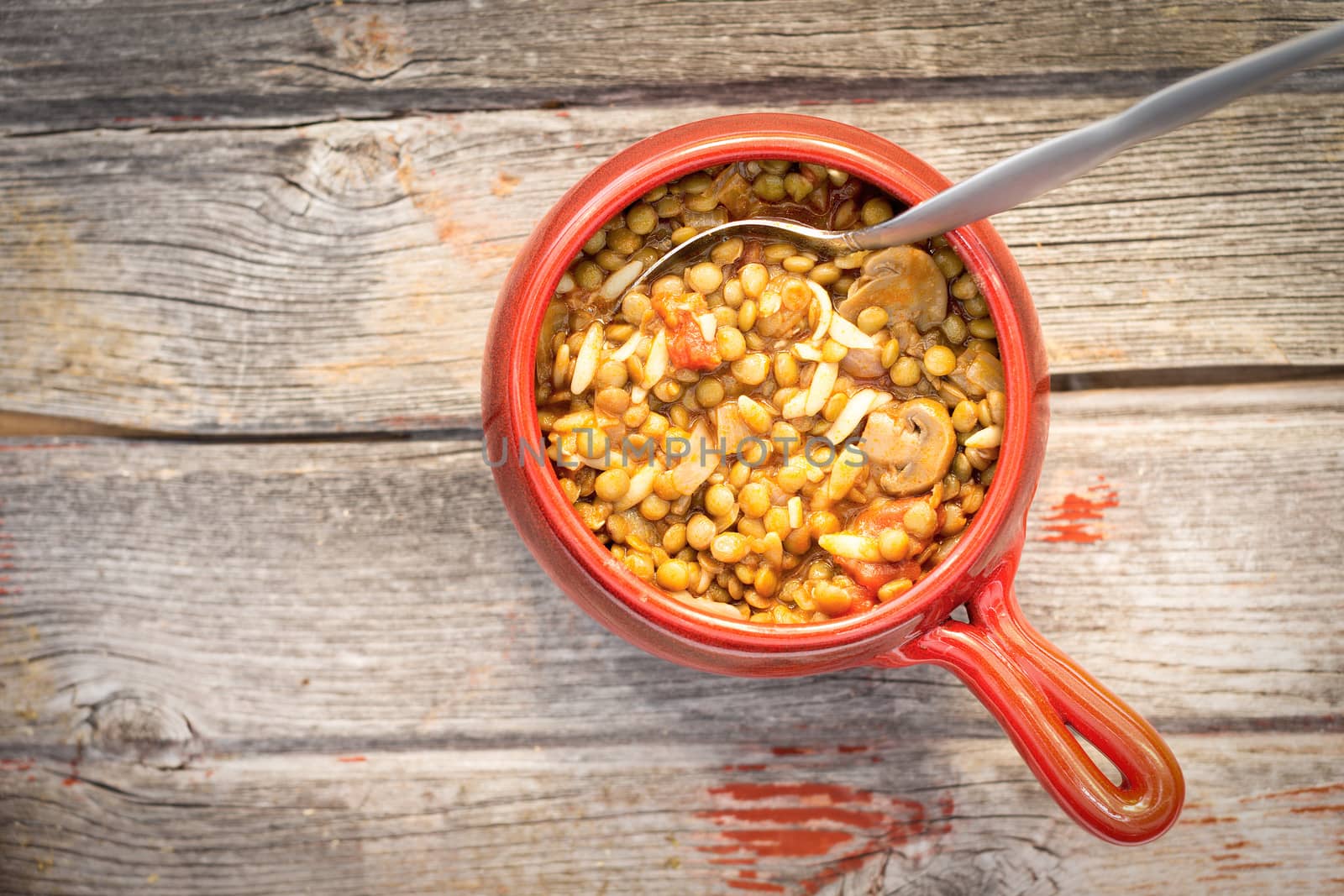 View from above of a bowl of hot nutritious lentil and mushroom soup to be served as a delicious starter to a winter meal standing on rustic wooden boards with copyspace