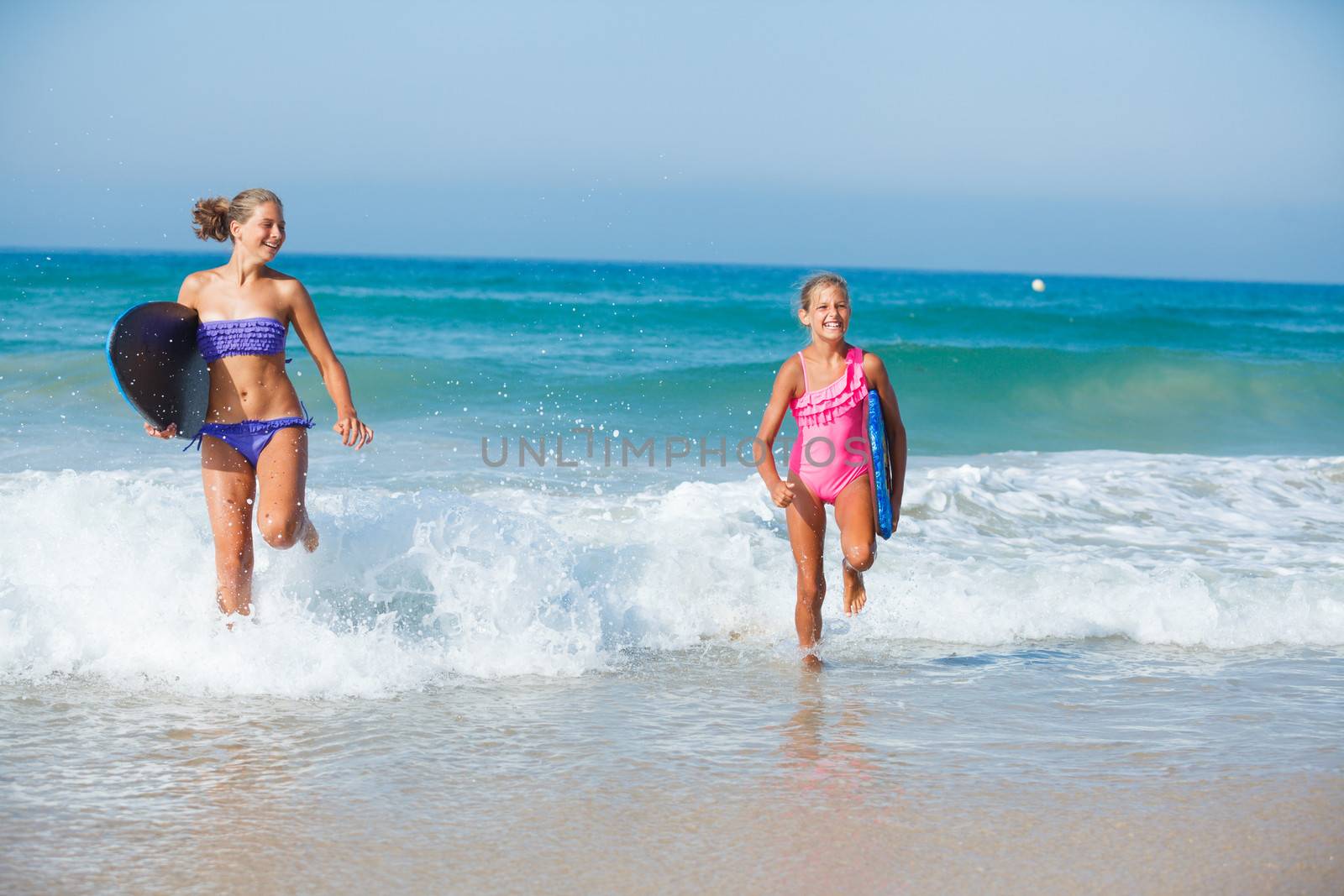 Two cute girls in bikini with surfboard running from the ocean