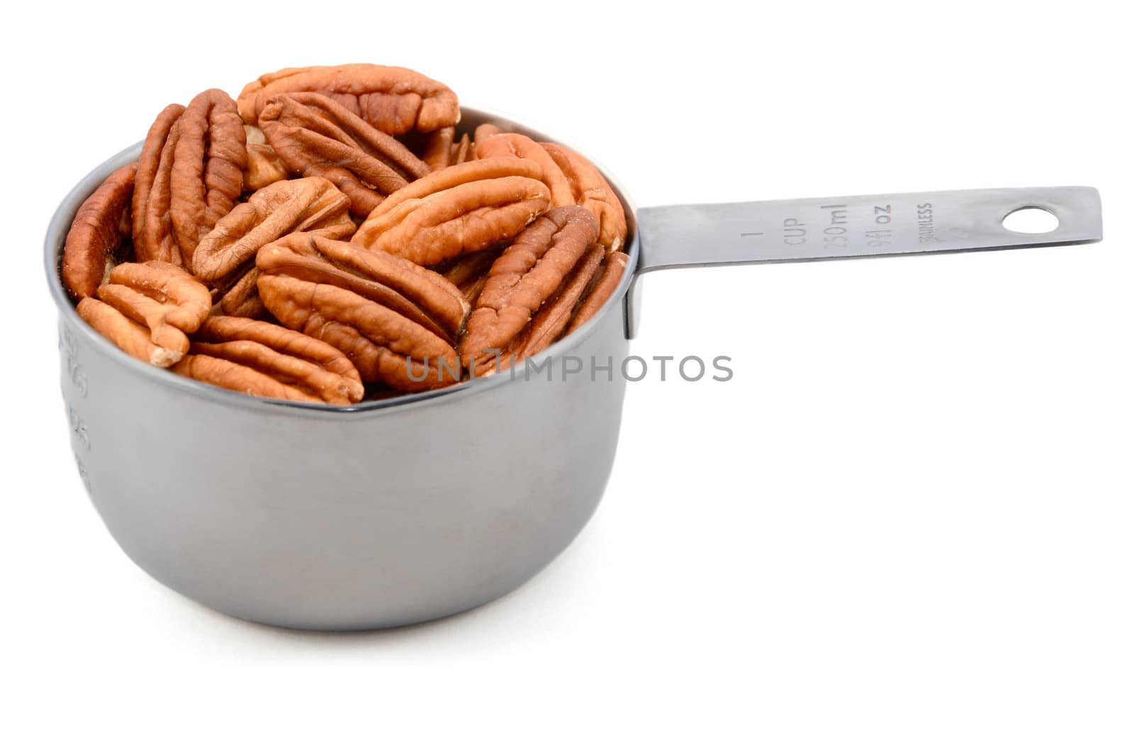 Whole pecan nuts in a metal cup measure, isolated on a white background