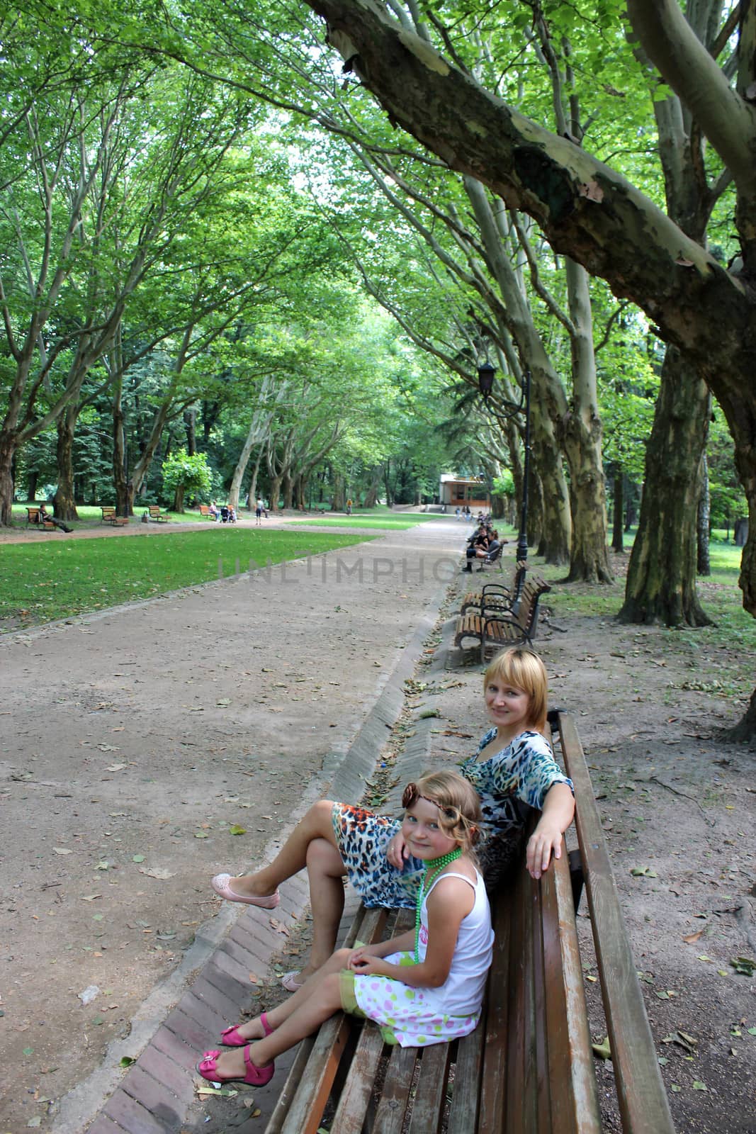 mother and daughter sitting on the bench in park by alexmak