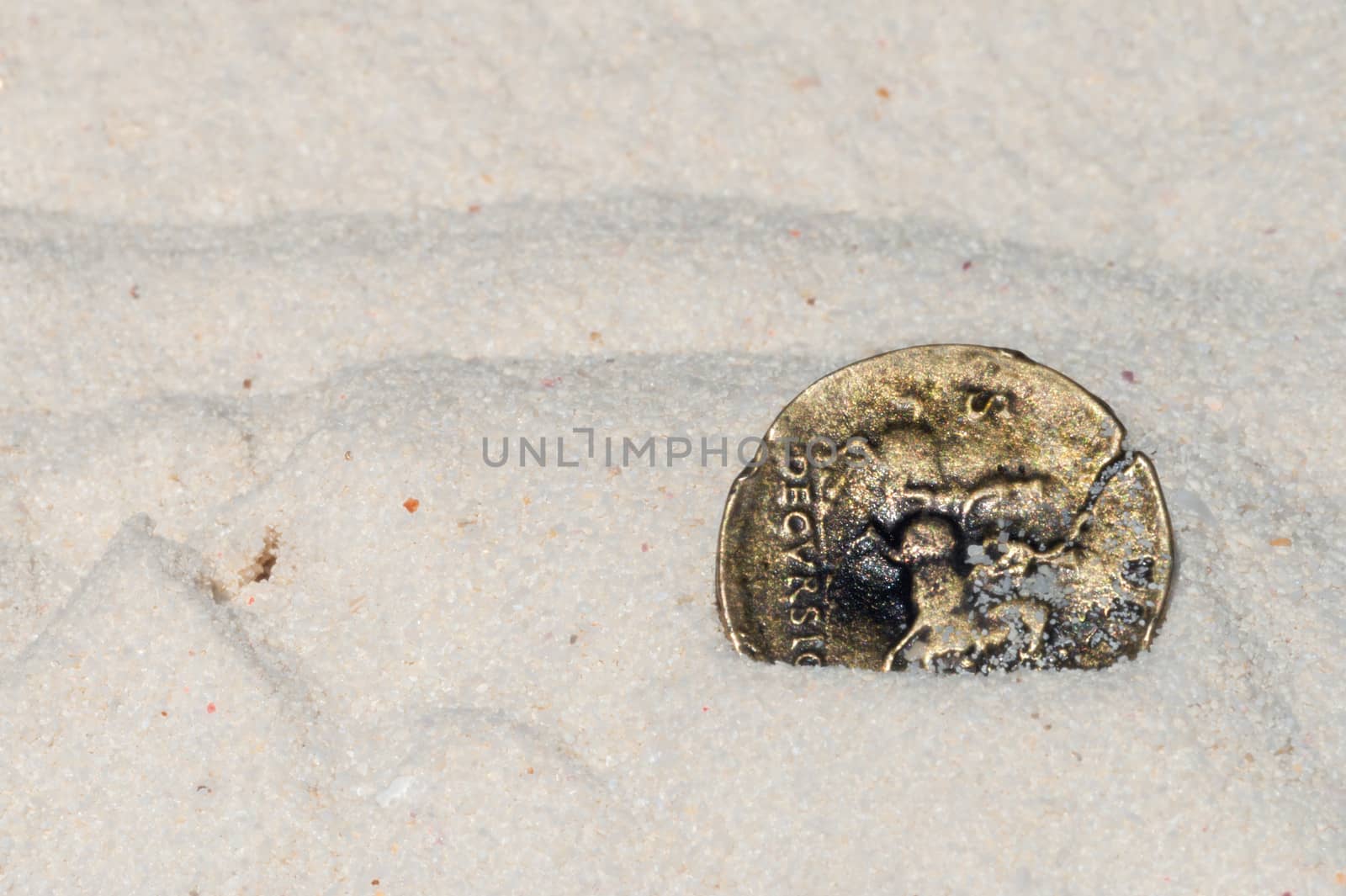 Ancient gold coin on sandy beach of tropical island