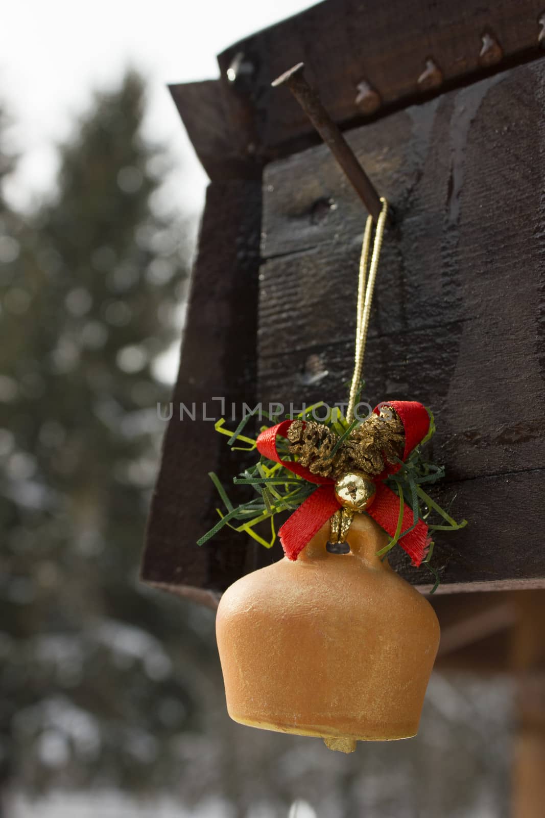 Toy bell pinned on a wooden frame with melting snow water drops running down.