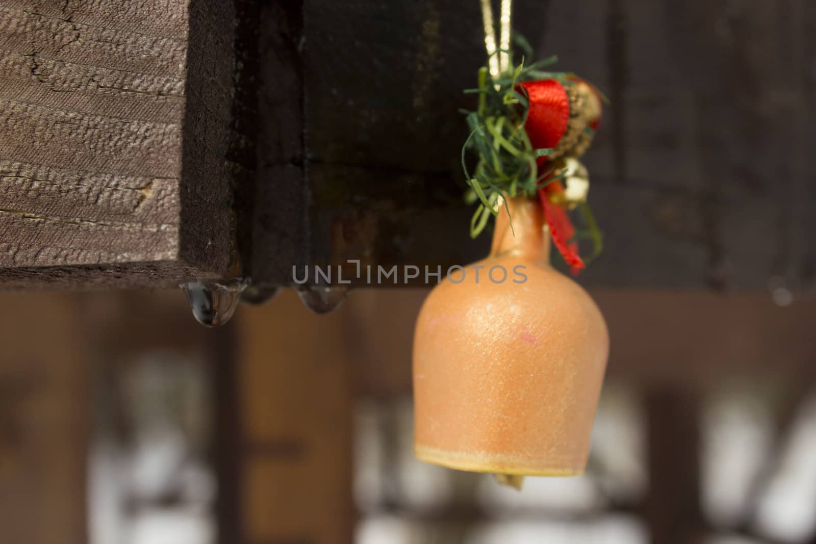 Toy bell pinned on a wooden frame with melting snow water drops running down.