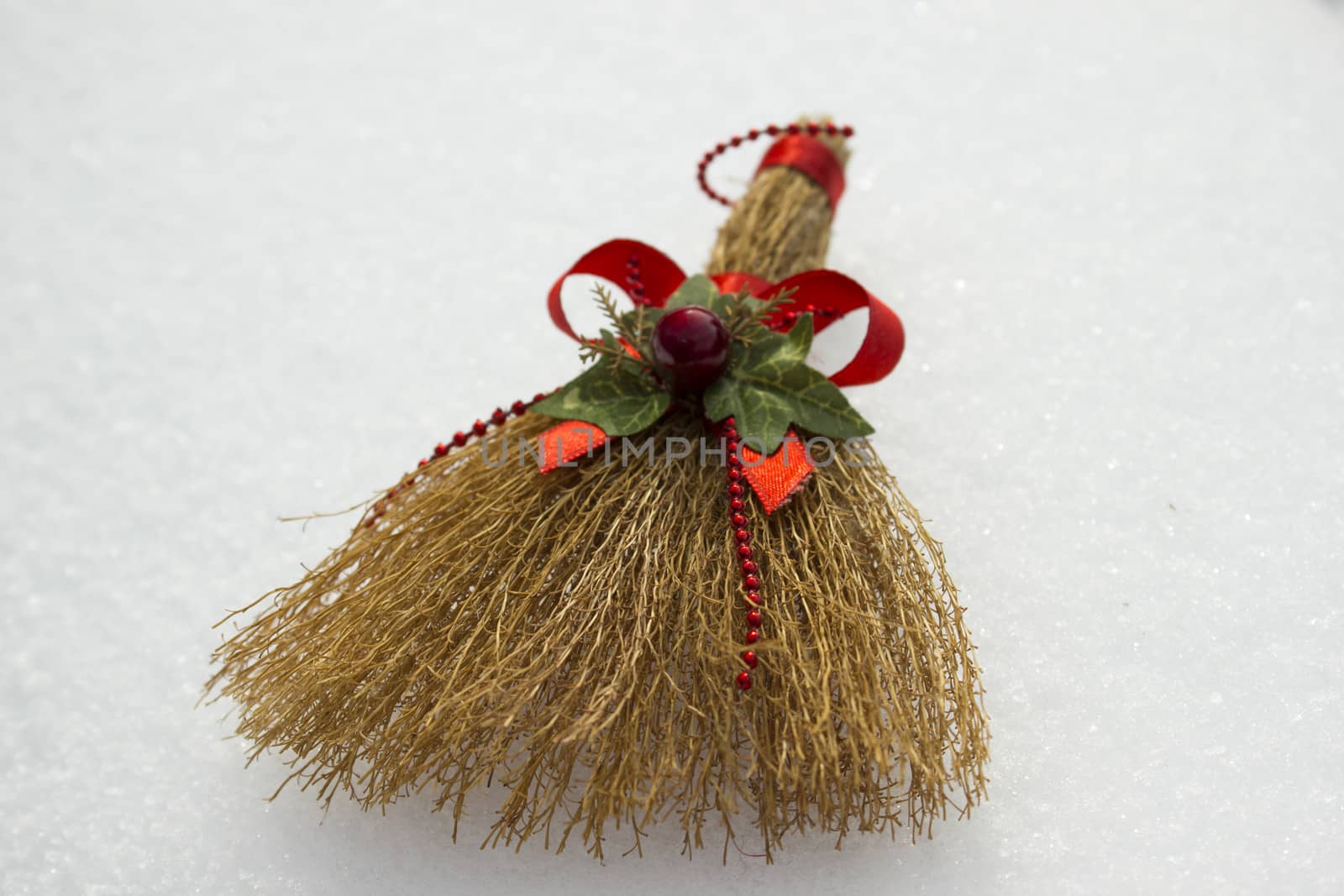 Toy broom with red ribbon and holiday ornaments laying around the snow.