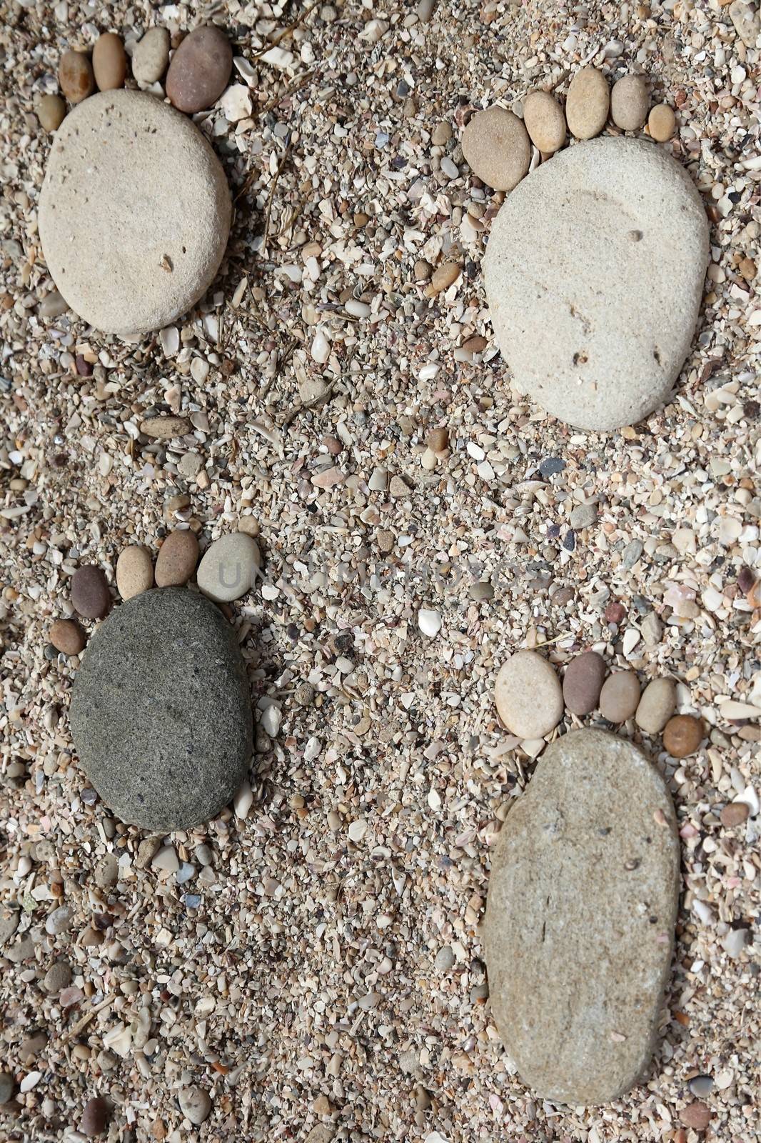 Smooth beach stones on the sand arranged to look like foot prints