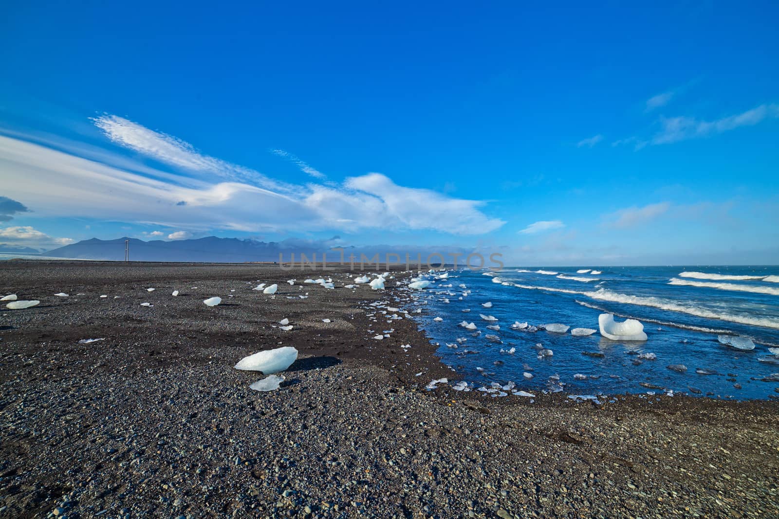 Beautiful beach in the South of Iceland with a black lava sand is full of icebergs from glaciers not far away.
