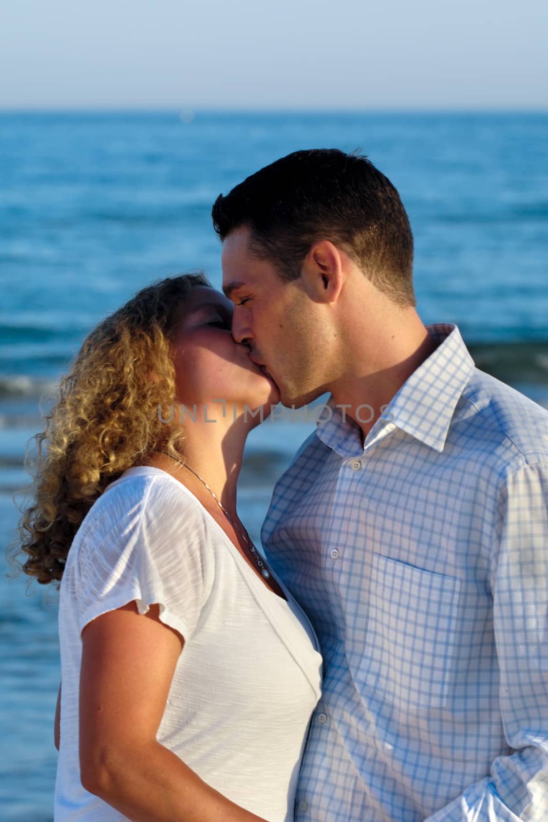 A young couple a standing near beach kissing.