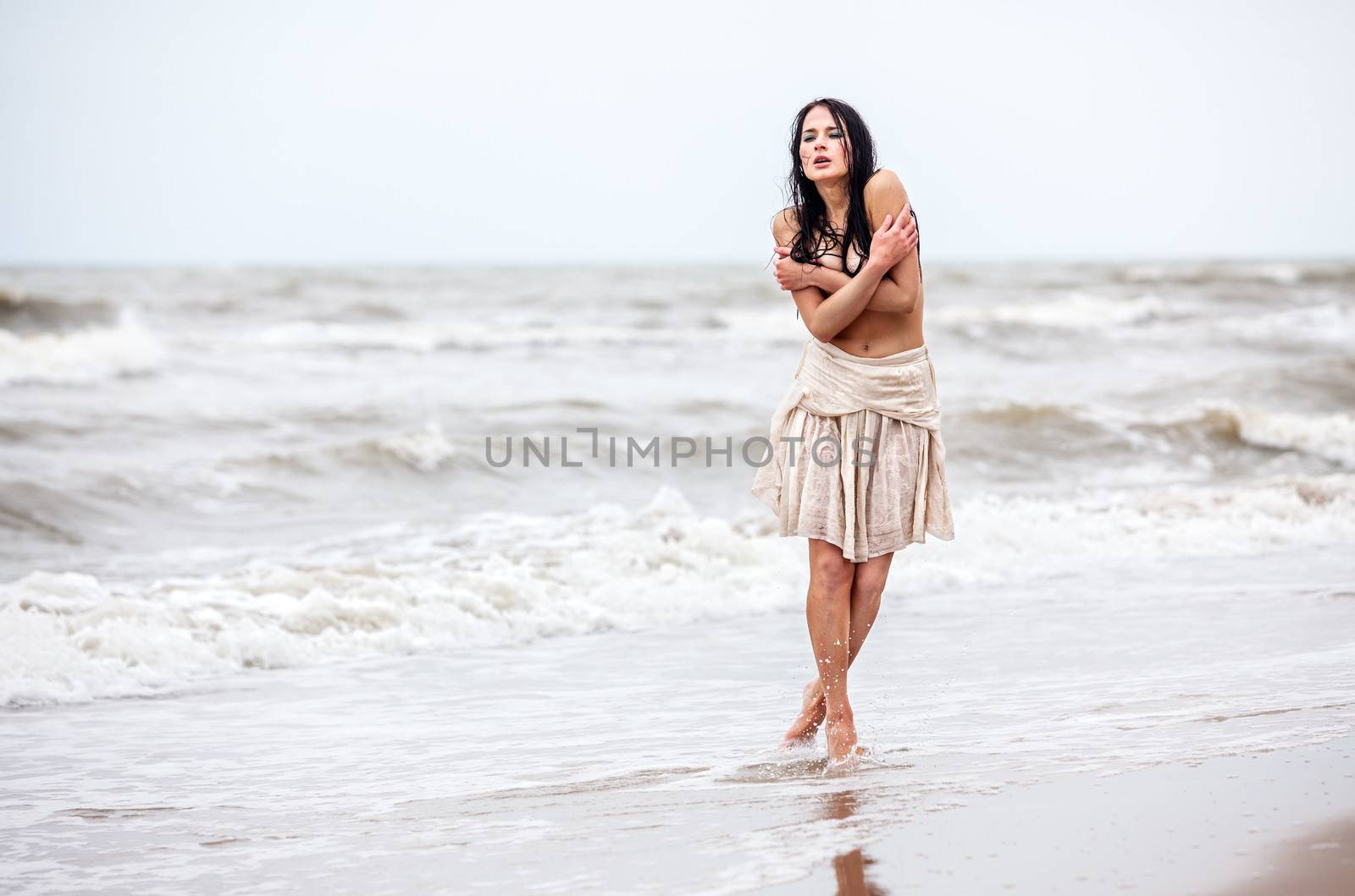 Beautiful young seminude woman in the cold sea waves