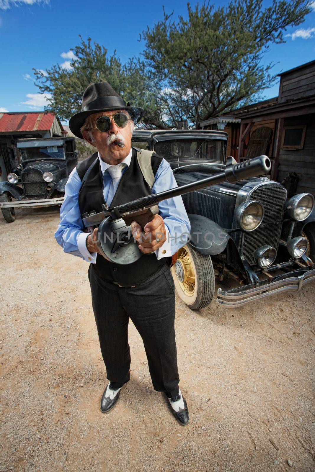 Male gangster with sunglasses, cigar and machine gun outdoors