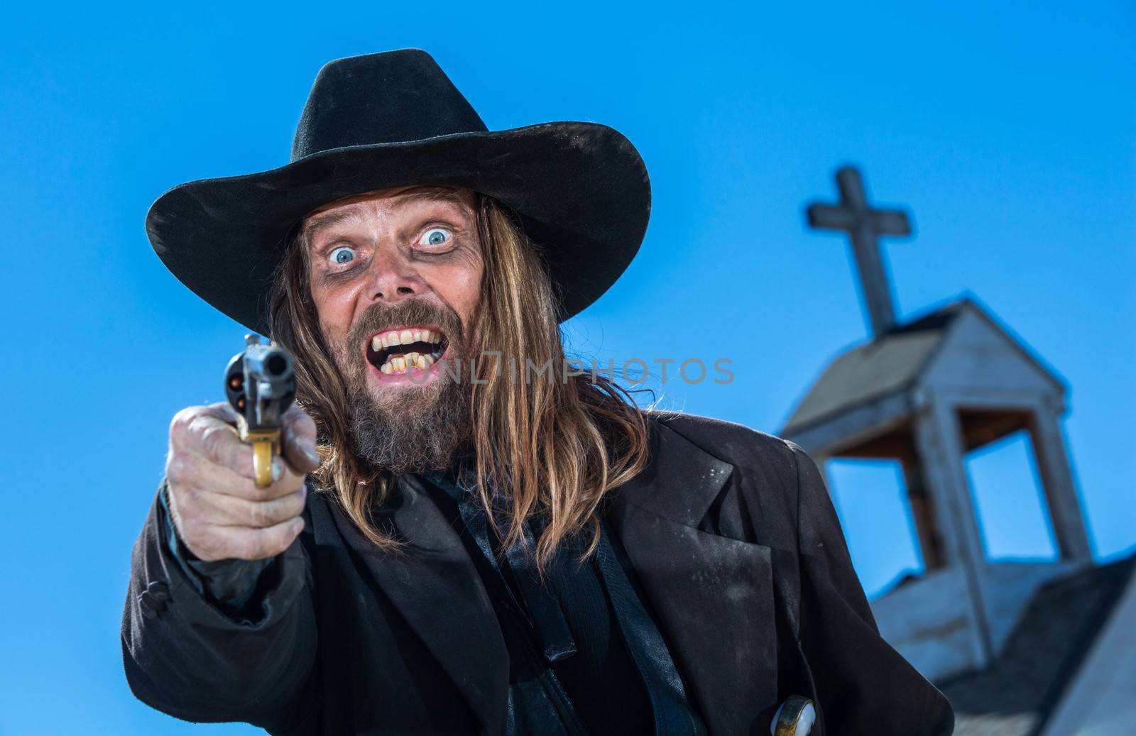 A laughing cowboy holding a gun near a church