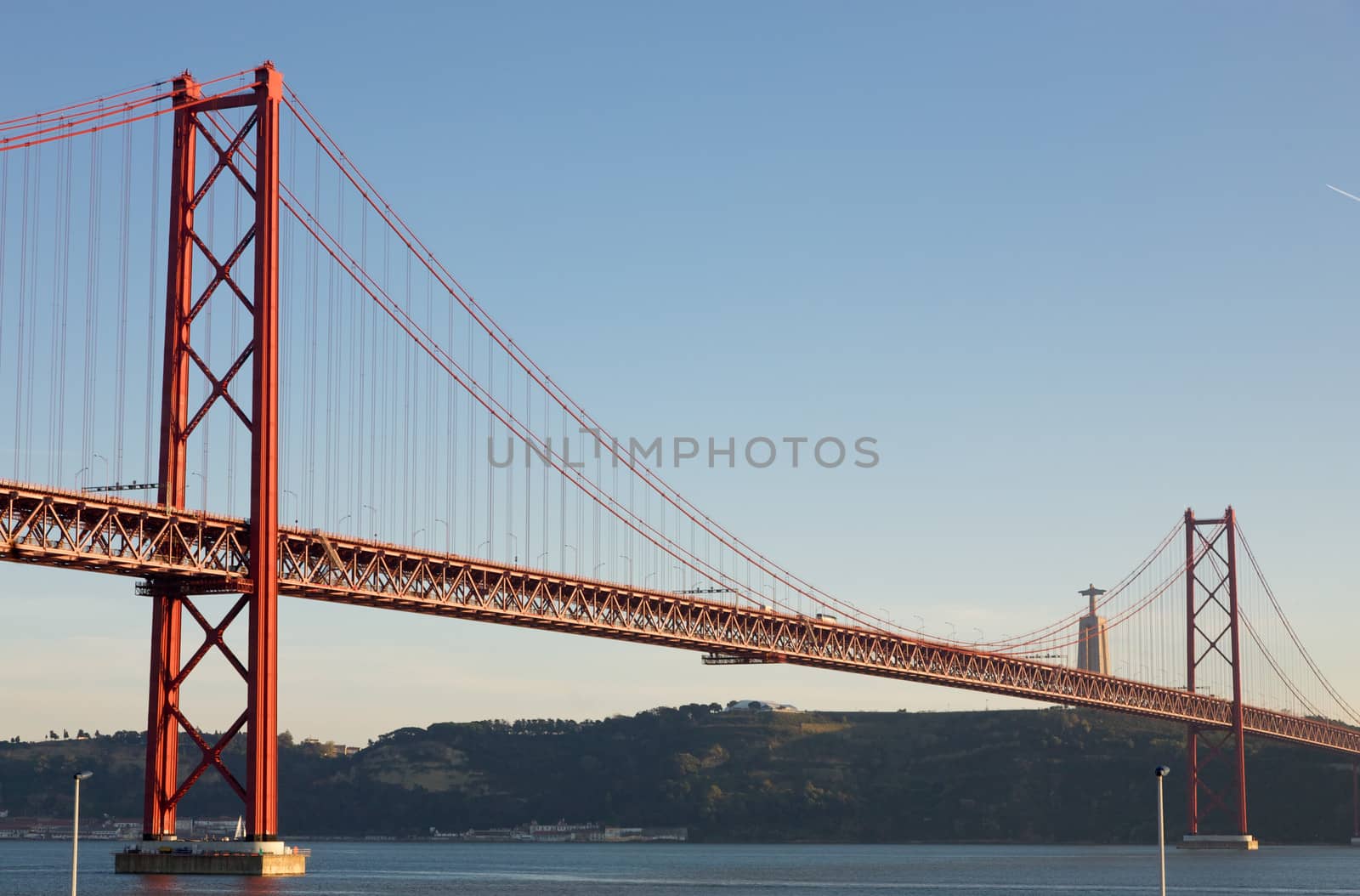 View of the April 25th Bridge in Lisbon, Portugal. This bridge is connecting Lisbon to the municipality of Almada on the south bank of the Tagus River. Statue of Jesus in the background.