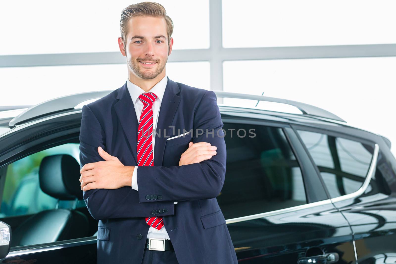 Young man or auto dealer in car dealership by Kzenon