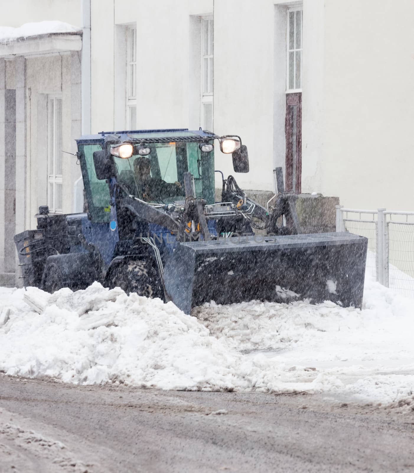 Snowplow cleaning a city street in snowfall by juhku