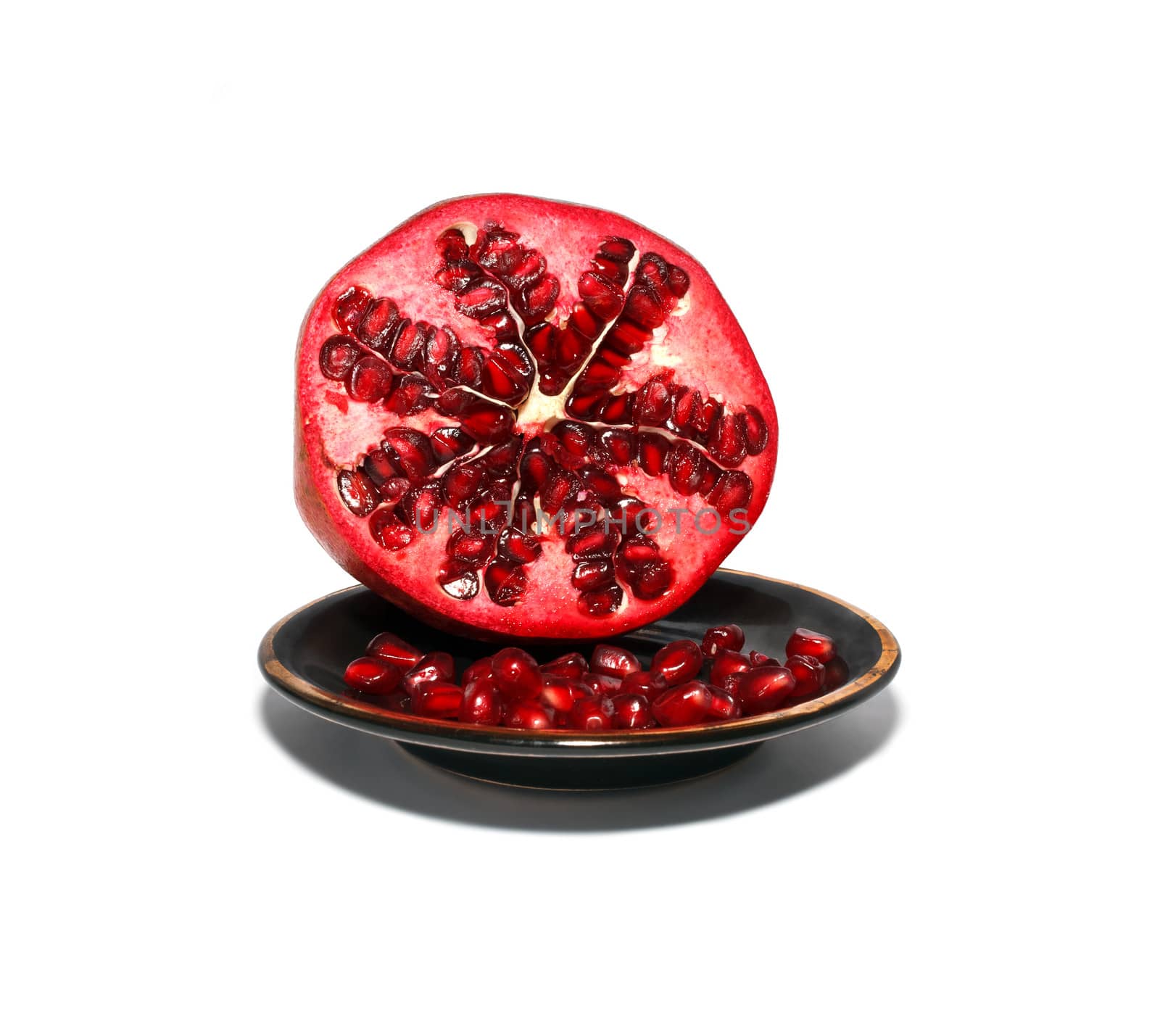 Seeds and sliced pomegranate on a black saucer on a white background