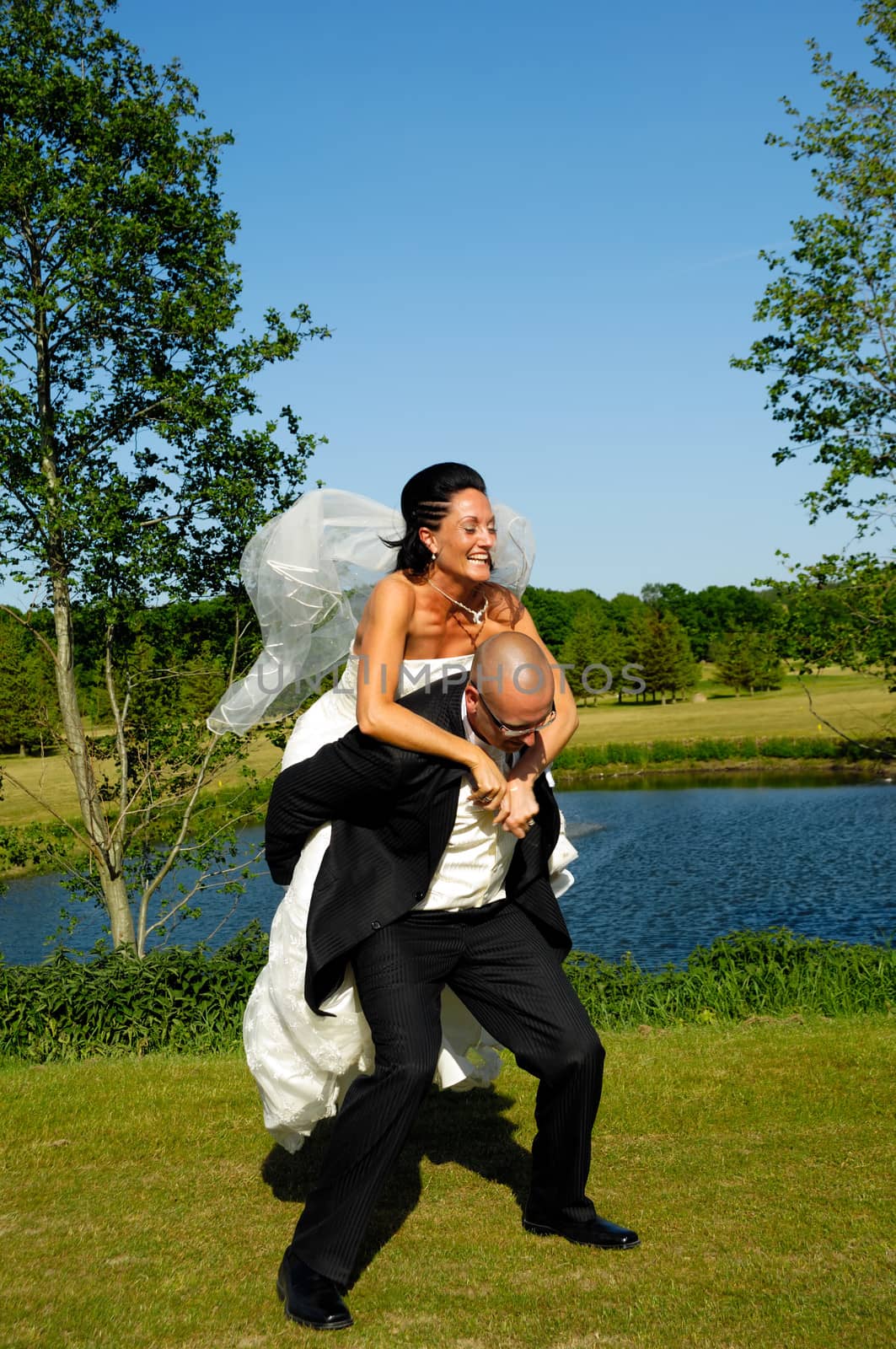 Groom is lifting his bride up in a park.