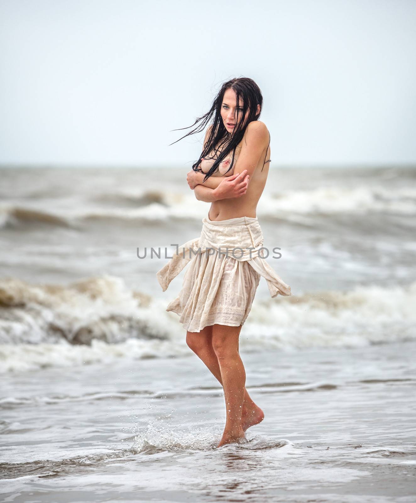 Beautiful young seminude woman in the cold sea waves