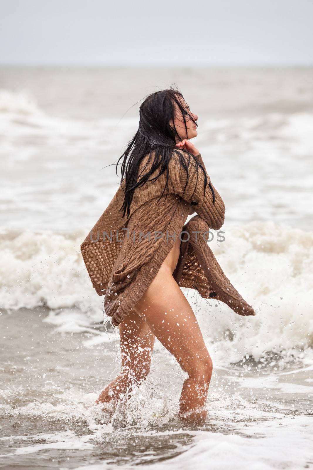 Beautiful young seminude woman in the cold sea waves