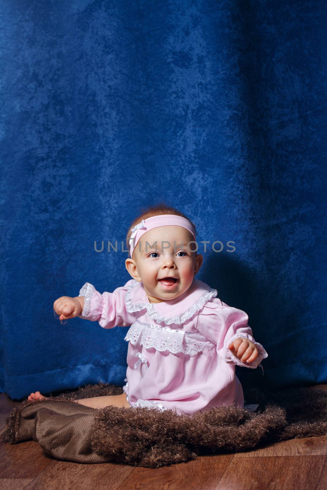 Pretty blue-eyed girl in a pink dress sitting on the floor