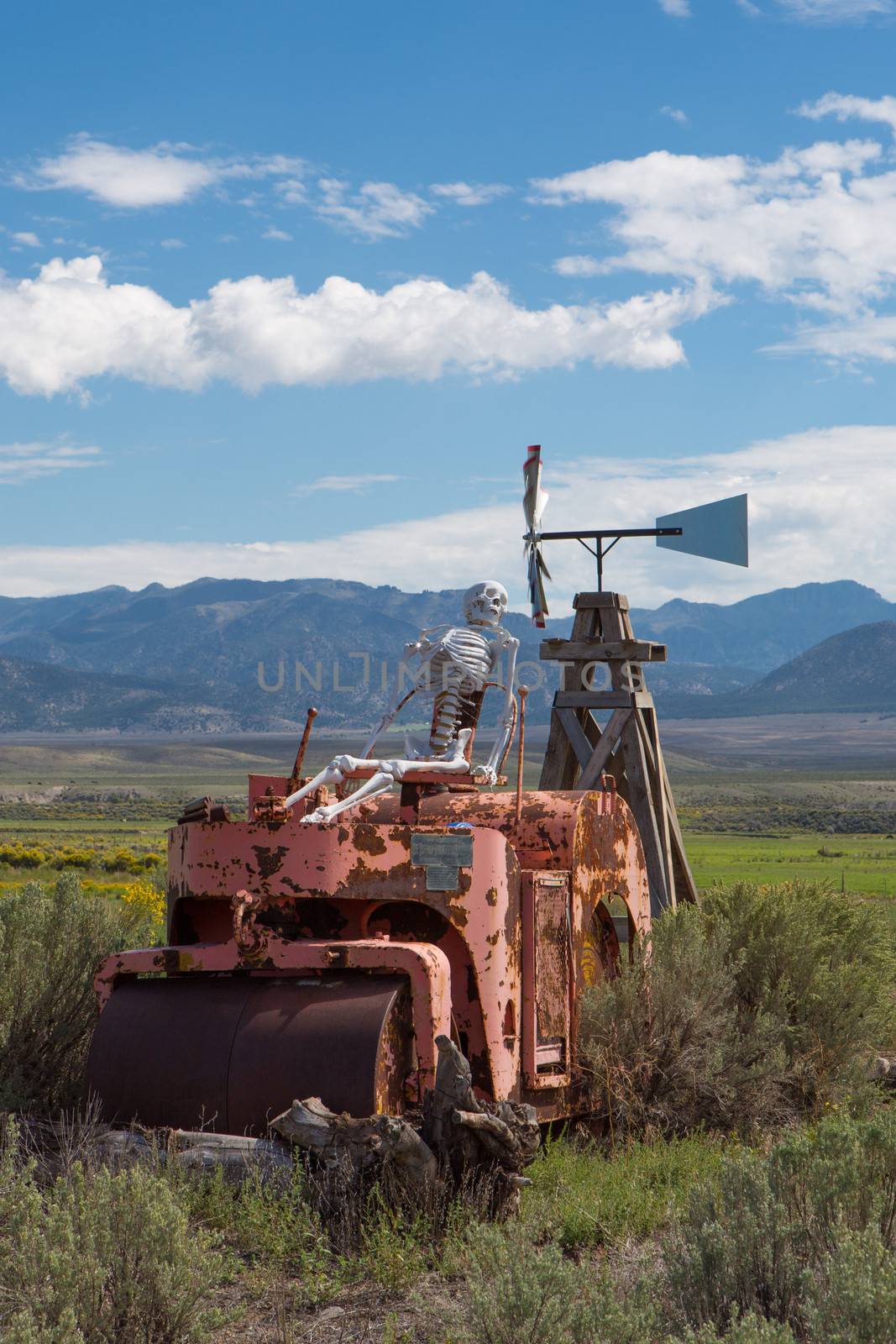 Skeleton sitting on a vintage tractor in Utah with mountains in the background.