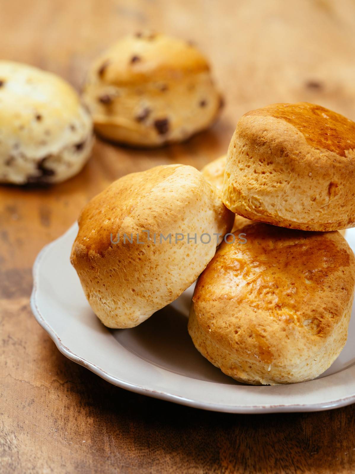 Photo of delicious plain scones on a plate.  Two chocolate scones in the background.