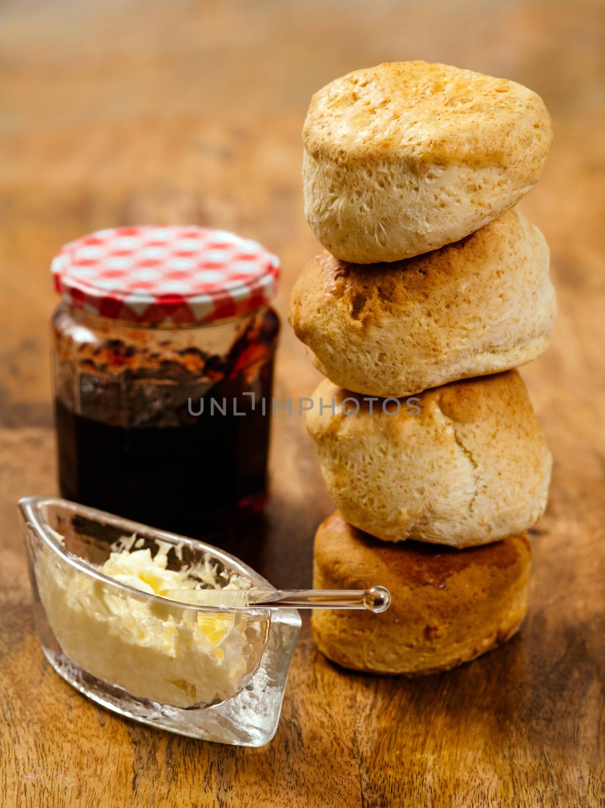 Photo of delicious scones stacked on a table with clotted cream and jam.
