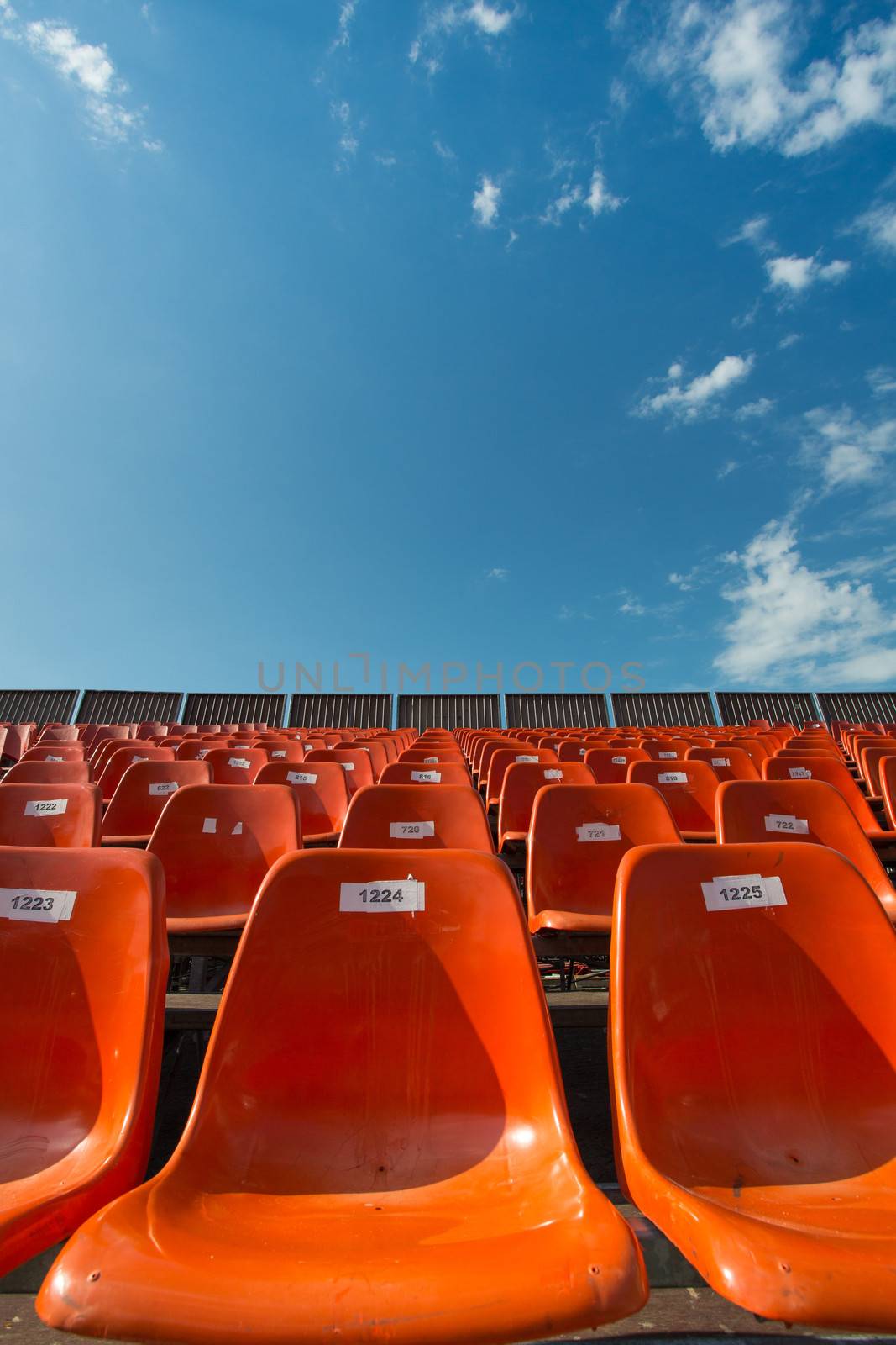 Lots of orange seats at an outdoor venue with a blue sky