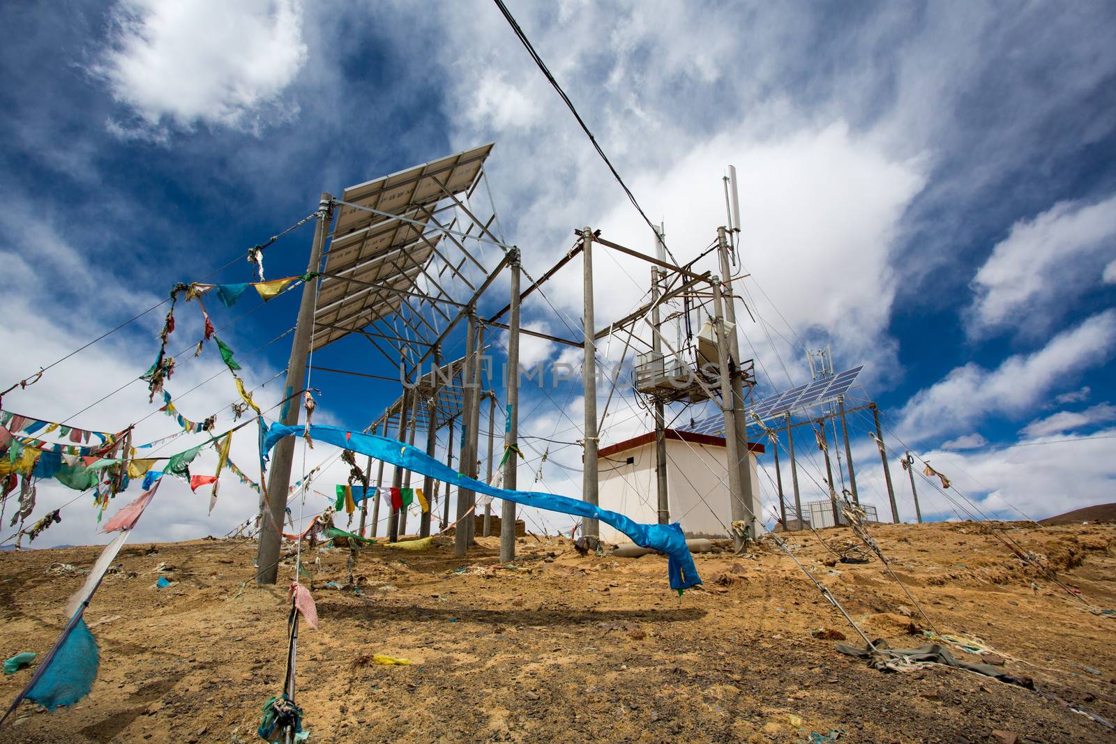 Telecomunication instalation at the top of a mountain in Tibet with prayer fabrics under a blue sky.