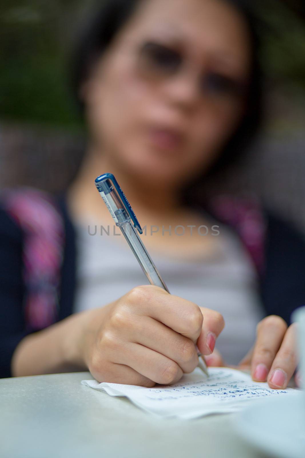 Close-up of a Chines woman writing a letter on a table. by watchtheworld