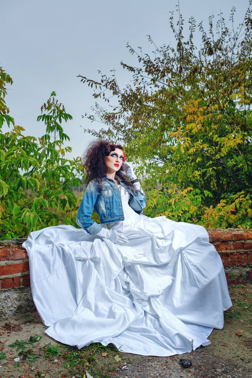 Beautiful bride in wedding dress and denim jacket in autumn park