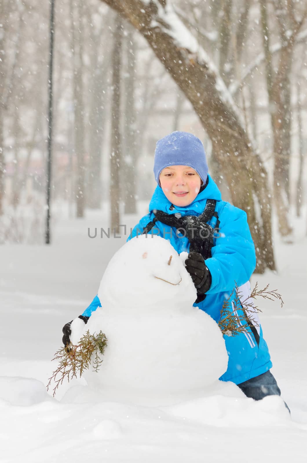 boy makes a snowman in park