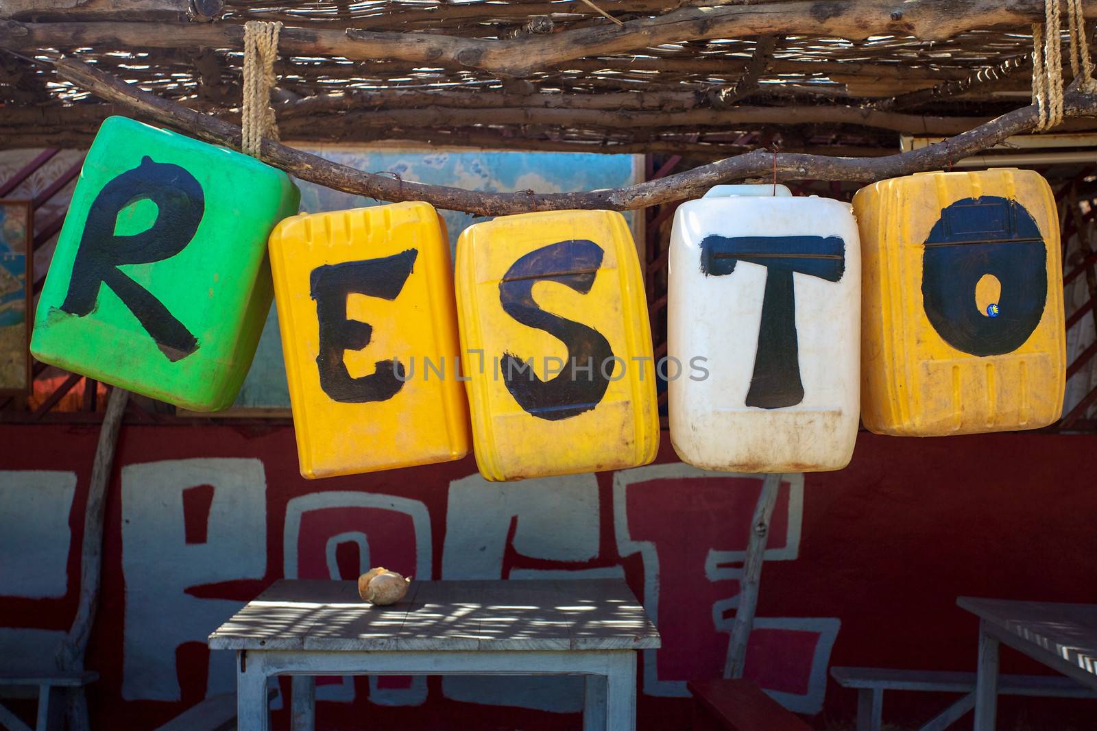 Letters resto or restaurant written on plastic colored buckets with empty wood table in Saint-Louis, Senegal.