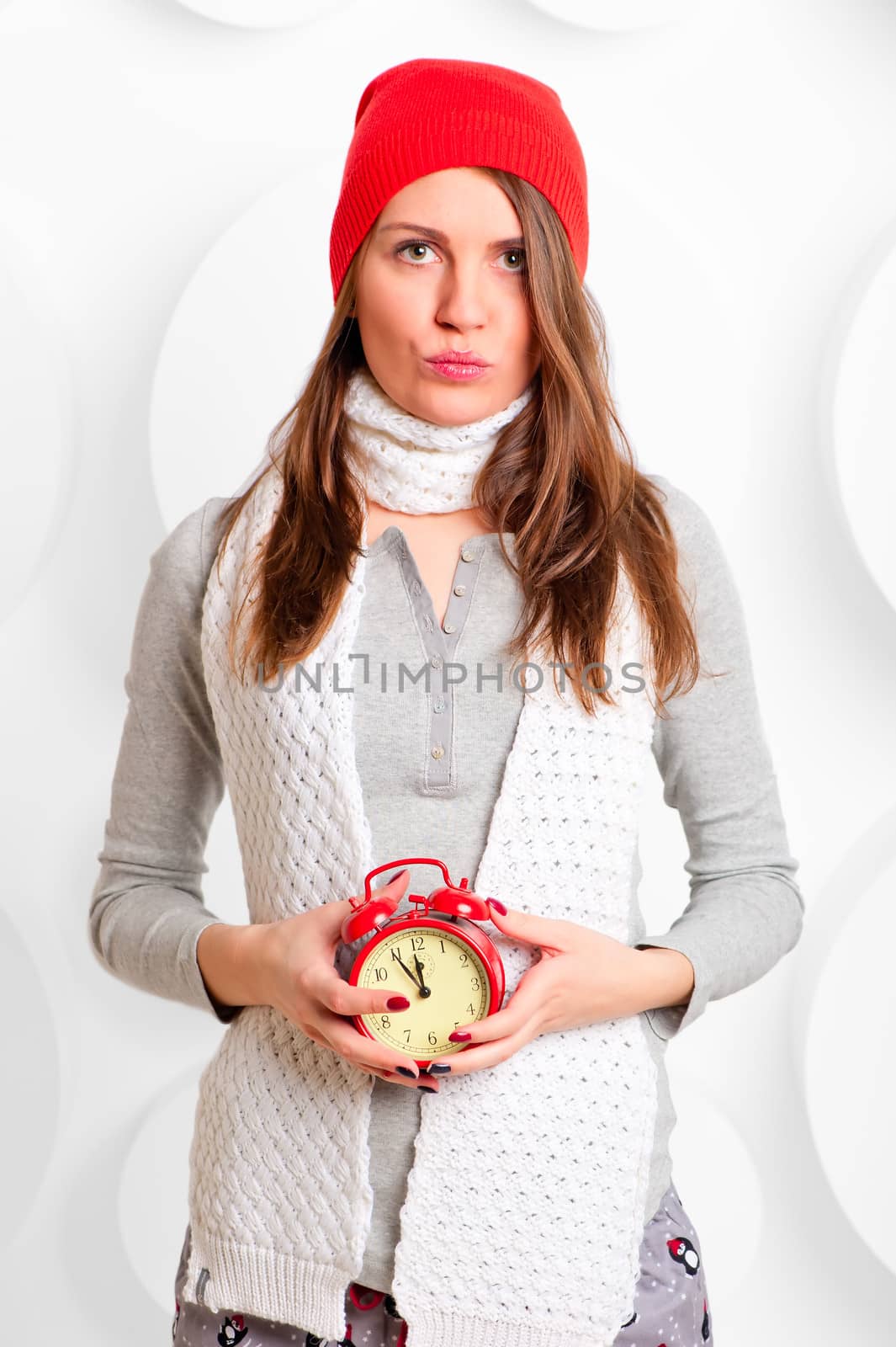 girl in a hat and scarf with red alarm clock