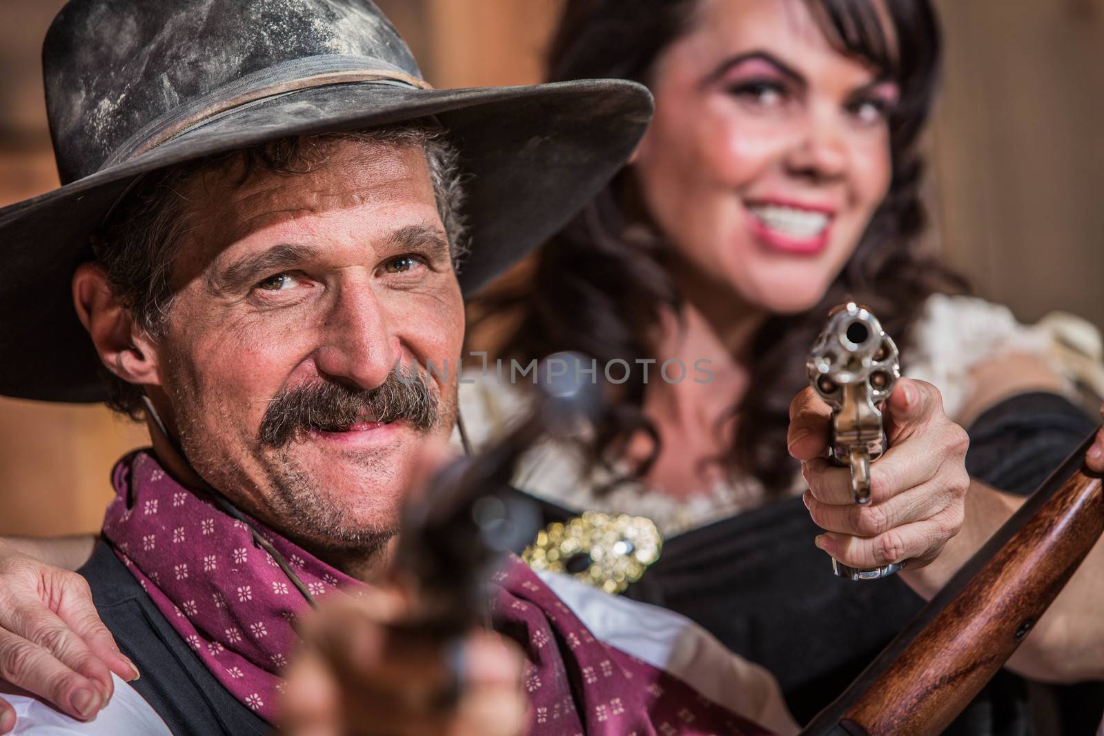 A Smiling Cowboy and Saloon Girl Point Their Weapons at You