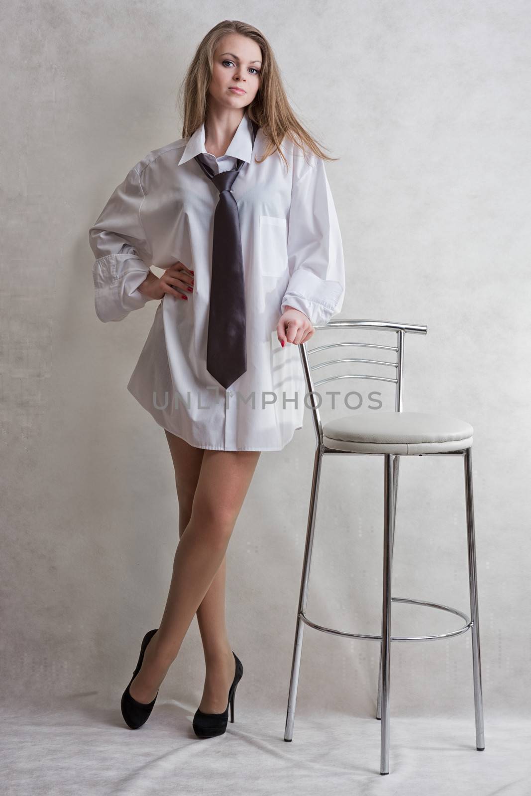 Young sexy girl the blonde in a man's white shirt and dark tie with bar chair