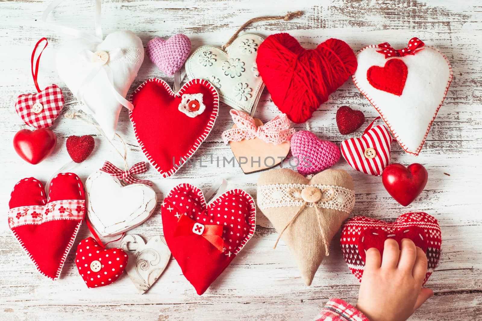 Valentine handmade hearts on the shabby wooden table and child's hand