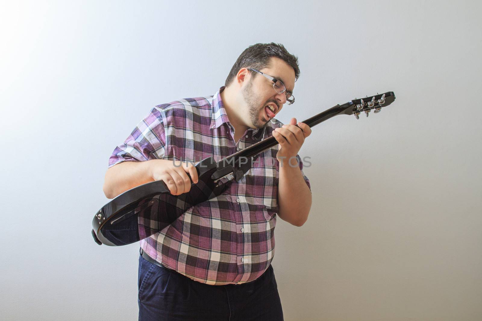 Overweight man about to lick the string of a guitar