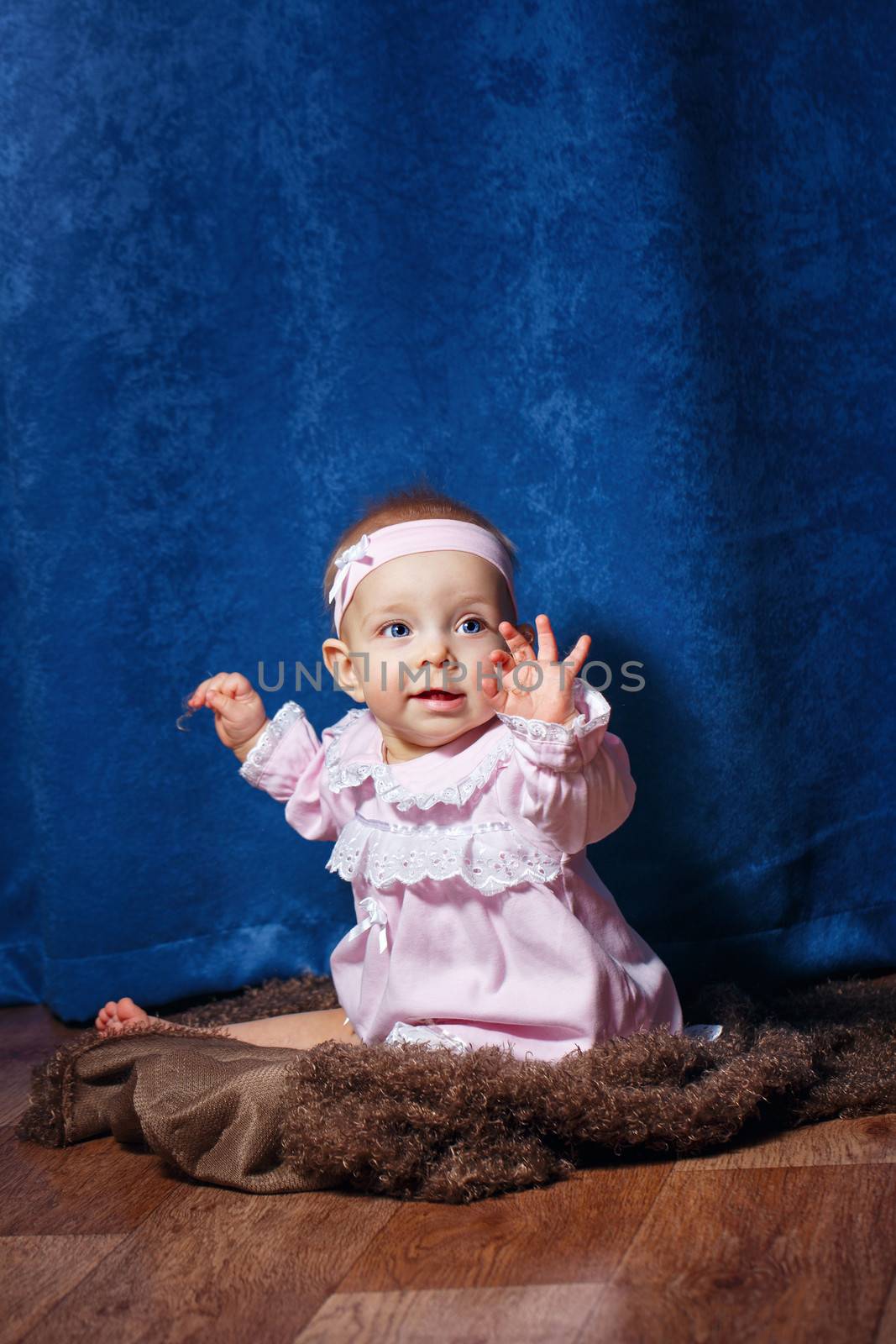 Pretty blue-eyed girl in a pink dress sitting on the floor