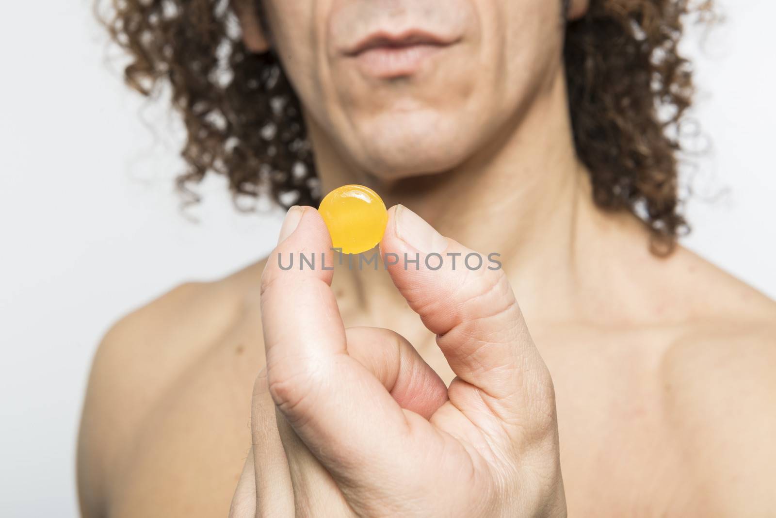 Cropped shot of bare chested mediterranean man holding colourful pill
